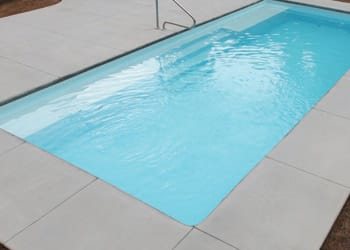 Rectangular fiberglass pool with clear turquoise water and tiled deck in a sunny backyard