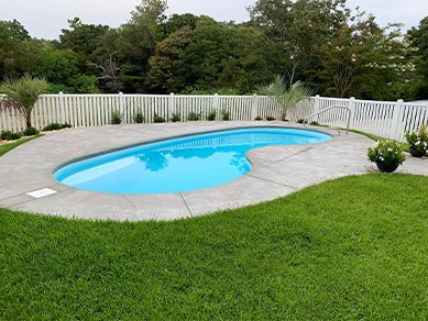 Fiberglass pool in a sunny backyard with a white picket fence